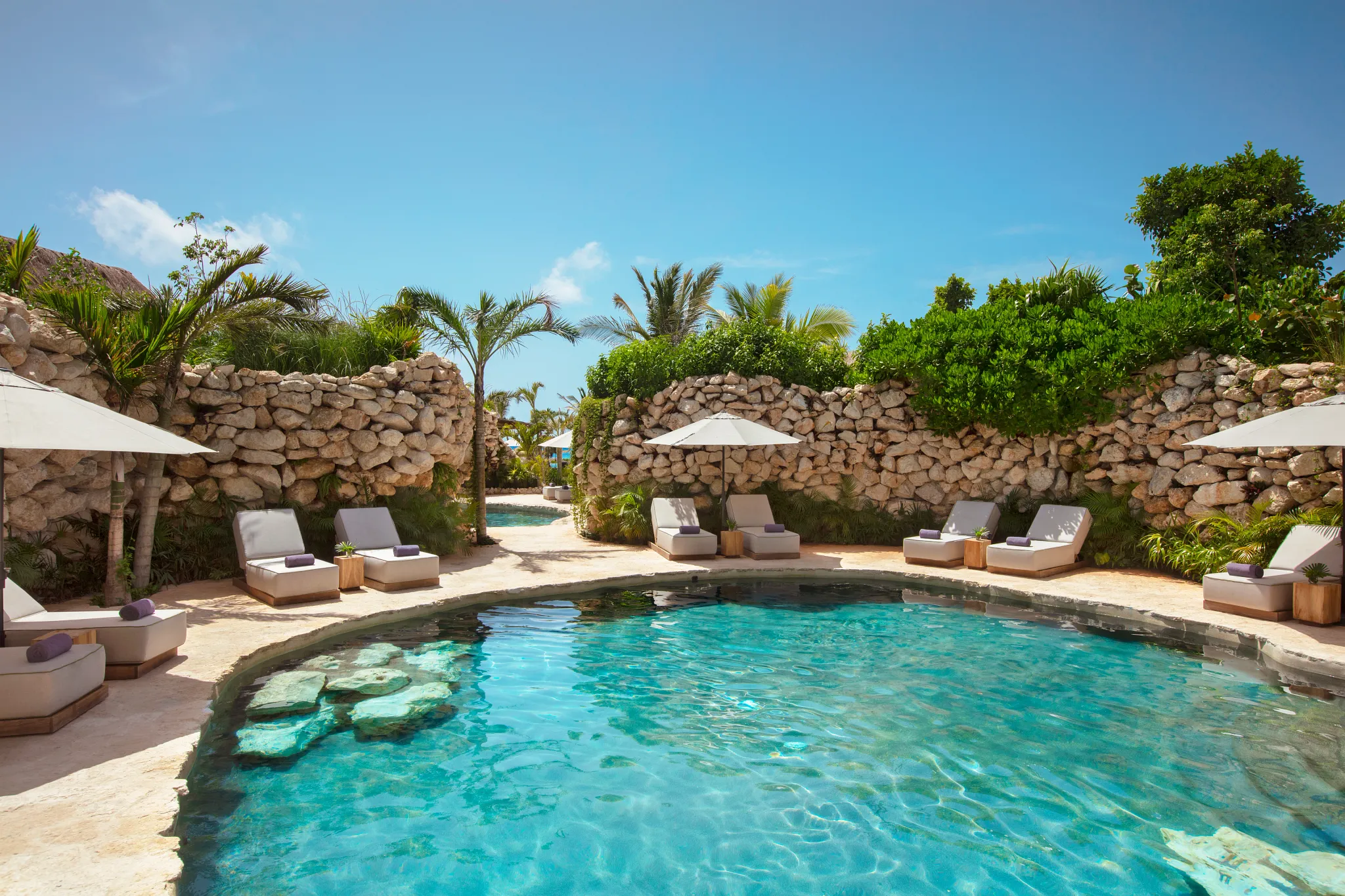 Cenote-style pool surrounded by natural stone walls and lounge chairs at Secrets Moxché Playa Del Carmen.