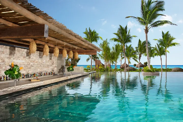 Sugar Reef Pool Bar at Secrets Moxché Playa del Carmen featuring a swim-up bar beside an ocean-view infinity pool with palm trees.