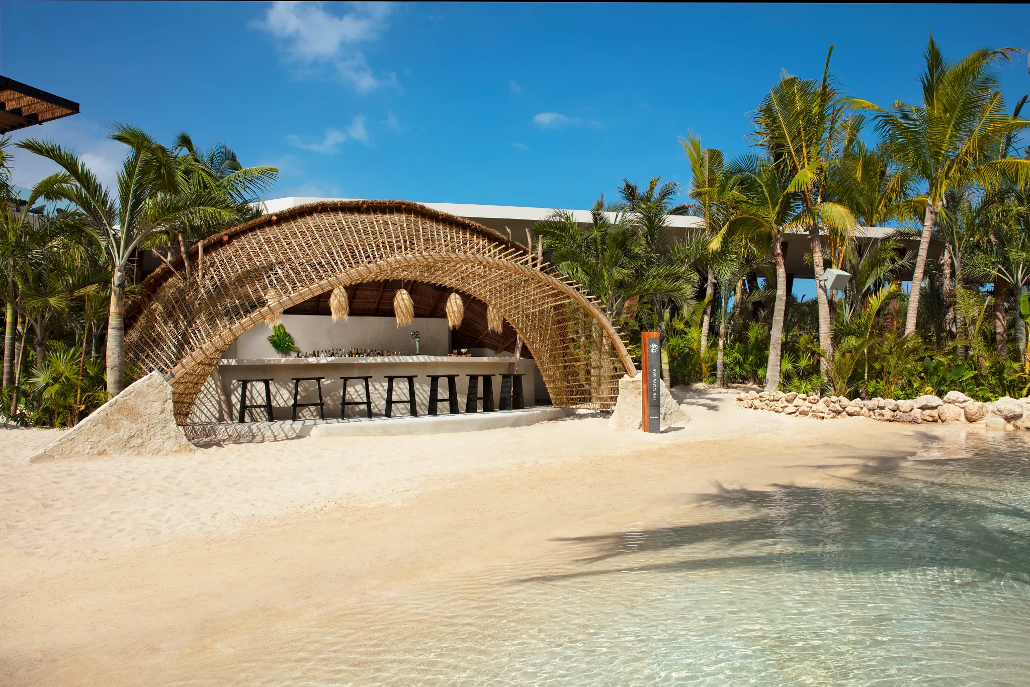 The Cove Bar at Secrets Moxché Playa del Carmen featuring a tropical beach pool bar with a curved bamboo canopy beside a lagoon-style pool.